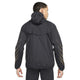 En person kigger væk fra kameraet iført Nike Nk Rpl Jakob Jkt til mænd i Black/Black/Metallic Gold - en let, vandafvisende løbejakke med hætte, afslappet pasform og tynde metalliske guldlinjer på ærmerne.