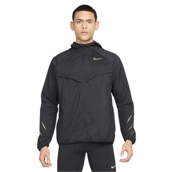 En person står med ansigtet fremad i en Nike Nk Rpl Jakob Jkt, Herre, Black/Black/Metallic Gold med Dri-FIT-teknologi, lynlås foran og guldfarvet swoosh-logo, sammen med sorte leggings på en almindelig hvid baggrund.