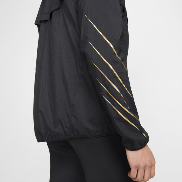 En person set fra siden er iført Nike Nk Rpl Jakob Jkt, Herre, Black/Black/Metallic Gold med fire tynde diagonale guldstriber på ærmet og sorte bukser på en ensfarvet baggrund. Kun armen og en del af overkroppen er synlig.
