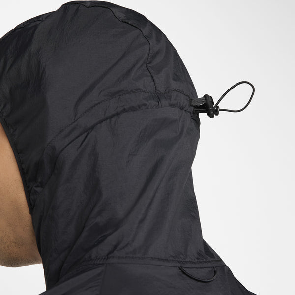 Nærbillede af siden og bagsiden af hovedet på en person iført Nike Nk Rpl Jakob Jkt, Herre, Black/Black/Metallic Gold, der viser en løbegang og en knap til at justere hættens pasform.