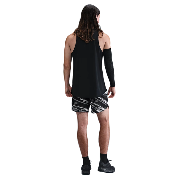 En person med langt hår står med ryggen til på en almindelig hvid baggrund iført en sort ærmeløs top, sorte sokker og sko, et sort ærme på højre arm og Nike Nk Df Stride 7In Bf Shrt Op2 shorts i Photon Dust/Reflective Silver.