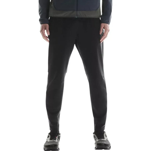 En person, der ser fremad, iført en mørk jakke, On Weather Winter Pants Herre Black og sorte løbesko. Billedet er beskåret fra brystet og ned for at fremhæve underkroppen og bukserne.