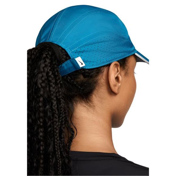 En person med langt, krøllet hår, der er trukket gennem åbningen bagpå en grøn Nike Adv Fly Cap, ses bagfra. Denne unisex-kasket har et lille hvidt mærke, et perforeret svedtransporterende design og er sat sammen med en sort top.