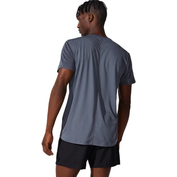 En person iført en ASICS Core SS Top, Herre, i farverne Carrier Grey og sorte shorts står med ryggen til kameraet foran en ensfarvet hvid baggrund. Denne kortærmede trøje byder på både komfort og stil til aktivt brug takket være det hurtigtørrende materiale.