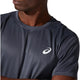 En person iført en Asics Core SS Top, Herre i farven Carrier Grey, en hurtigtørrende løbetrøje med et hvidt Asics-logo på brystet. Personen er afbildet fra skuldrene og opefter, med blikket let vendt mod venstre.