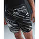 En person er iført Nike Nk Df Stride 7In Bf Shrt Op2 herre løbeshorts i Photon Dust/Reflective Silver og en sort langærmet top, mens han står med den ene arm langs siden. Billedet er beskåret fra midt på torsoen til midt på låret, hvilket fremhæver shortsene.