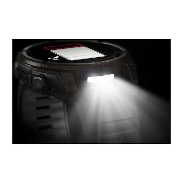 Et nærbillede af et Garmin Fenix 8 Solar Sapphire Titanium 51mm i Carbon Grey med Pebble Grey silikonerem viser, at den lyse hvide lommelygte er tændt og delvist oplyser urskiven i safirtitanium med digitale elementer.