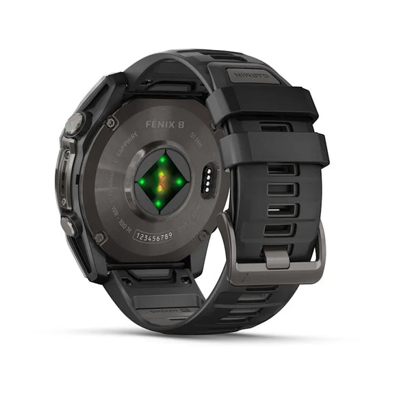 Et nærbillede viser bagsiden af et sort Garmin Fenix 8 Amoled Sapphire 51 mm (Carbon Grey DLC) smartwatch med aktiveret sensorlys, justerbar Pebble Grey silikonerem og indgraverede modeldetaljer på kabinettet.