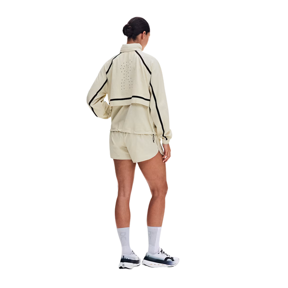 En person står med ryggen til og har en ON Performance Volt-jakke (Dame, Hare) på sammen med matchende shorts med sorte detaljer, lange hvide sokker og sneakers. Jakken har ventilationshuller på ryggen. Baggrunden er ensfarvet hvid.