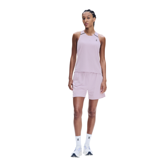 En person står med ansigtet vendt fremad iført en On Performance Tank, modellen »Dame« i farven »Foxglove/Orchid«, med matchende shorts, hvide sokker og hvide sportssko, foran en ensfarvet hvid baggrund.
