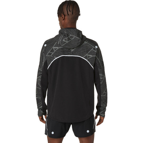 En person vender sig væk fra kameraet iført en Asics Limited Series Lite-Show Jacket, Herre, Performance Black med et geometrisk mønster og hvide detaljer samt matchende sorte shorts med ASICS refleks-teknologi.