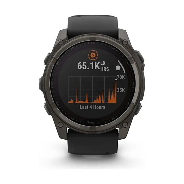 Et Garmin Fenix 8 Solar Sapphire Titanium 51 mm i Carbon Grey/Pebble Grey viser en skærm med en graf over de sidste 4 timers lyseksponering i orange, der viser 65,1K Lx HRS og en lodret skala fra 0 til 70K.