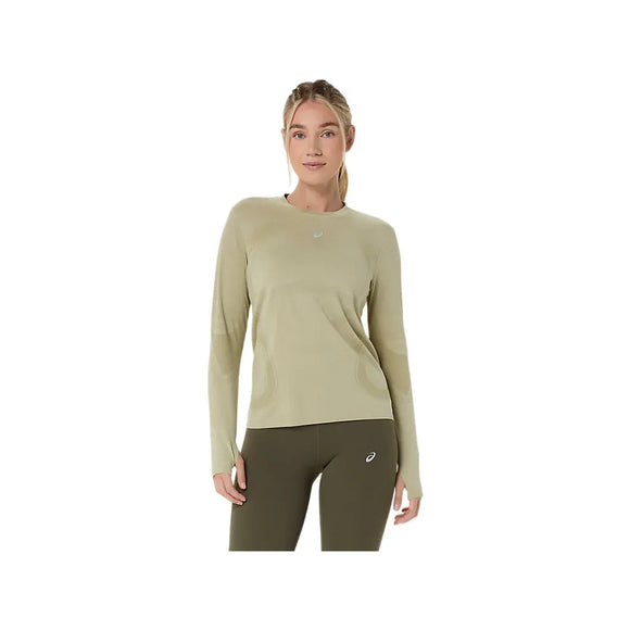 En kvinde med langt tilbagestrøget hår kigger fremad i en Asics Road Seamless LS Top til kvinder, Khaki/Cream, sammen med mørke olivenfarvede leggings. Hun poserer mod en almindelig hvid baggrund, der fremhæver denne åndbare løbetop.
