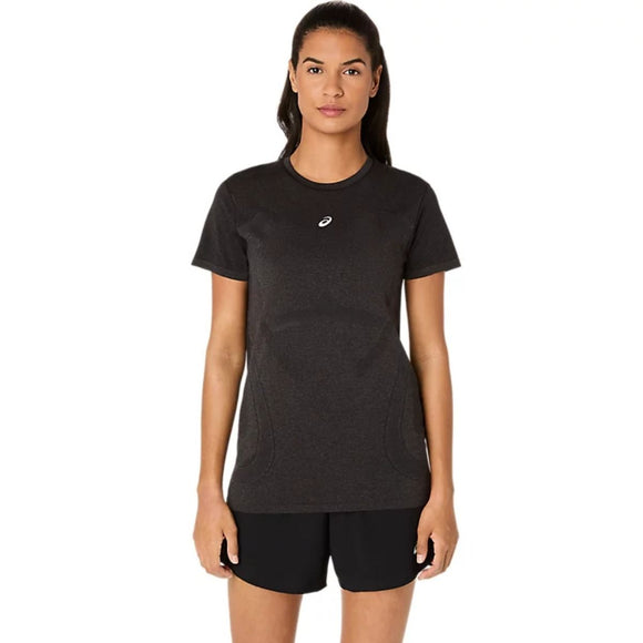 En kvinde står og kigger fremad iført en Asics Road Seamless SS Top til kvinder i Performance Black/Graphite Grey og sorte shorts på en almindelig hvid baggrund.
