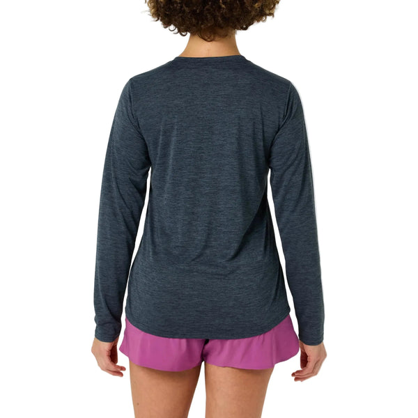 En person med krøllet hår ses bagfra iført en Patagonia Long-Sleeved Capilene Cool Daily Shirt for women i Smolder Blue - Light Smolder Blue X-Dye og pink shorts, stående mod en almindelig hvid baggrund med afslappede arme.