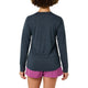 En person med krøllet hår ses bagfra iført en Patagonia Long-Sleeved Capilene Cool Daily Shirt for women i Smolder Blue - Light Smolder Blue X-Dye og pink shorts, stående mod en almindelig hvid baggrund med afslappede arme.