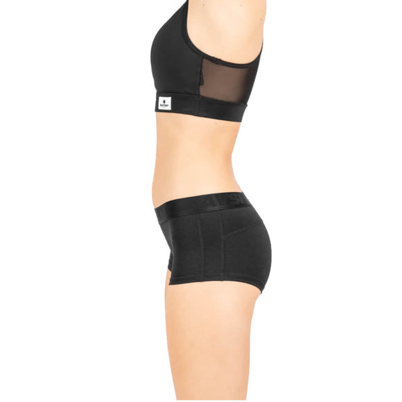 En person står i profil iført stretchundertøj - en sort sports-bh og Saysky Combat Hot Pants, Dame, Black - på en hvid baggrund. Billedet viser ikke hovedet eller underbenene.