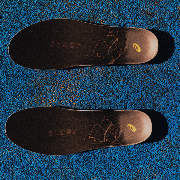 To Superblast 3-indlægssåler i farven Obsidian Grey fra Asics ligger side om side på en struktureret blå overflade. Hver indlægssål er forsynet med tallet 21.097 og et gult logo trykt tæt på hælen, hvilket henviser til deres højtydende design til løbesko. Der ses diskrete geometriske linjer, der minder om den avancerede FF LEAP™-skumstøddæmpning, som er unik for unisex-modellen Superblast 3 i farvekombinationen Obsidian Grey/Ice Mint.