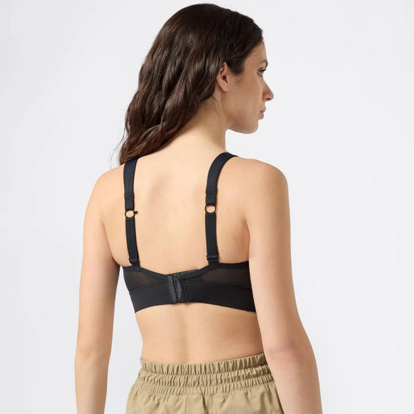 En kvinde med langt brunt hår ses bagfra iført Shock Absorber High Intensity Bra, Dame, i sort med justerbare stropper og beige bukser med elastik i taljen på en almindelig lys baggrund.