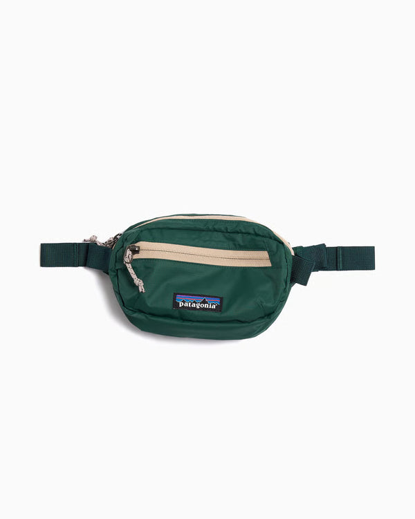Patagonia Terravia Mini Hip Pack i Cascade Green er en unisex bæltetaske lavet af genanvendt nylon ripstop med beige lynlås, frontlomme og justerbare mørkegrønne stropper, vist på en hvid baggrund.