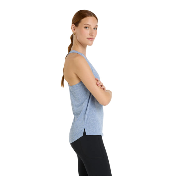 En kvinde med langt, rødligt hår, der er bundet tilbage, står sidelæns med armene over kors iført New Balance Athletics Tank til kvinder i Dusk Shower Heather og sorte leggings på en almindelig hvid baggrund.