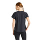 En kvinde med langt, flettet hår ses bagfra iført en New Balance Race Day Ultra Light T-shirt, Dame, Grey Matter og sorte bukser, stående på en almindelig hvid baggrund.