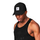 En mand i en sort tanktop og en Saysky Flow Logo Cap (unisex, sort) med et rektangulært logo på forsiden står på en hvid baggrund og kigger nedad.